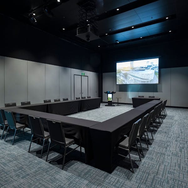 A sleek conference room arranged in a U-shape with dark tables and chairs, featuring a large screen at one end showing an image, emphasizing Te Pae’s modern design for meetings.